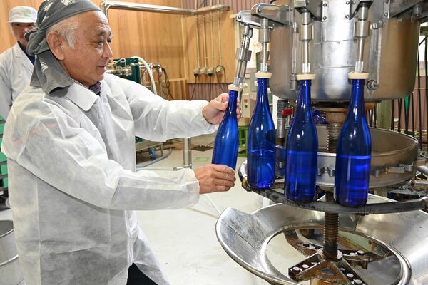 液体充填機のノズルに瓶を差し込み、酒を詰める筆者＝２月１１日、鹿沼市上粕尾