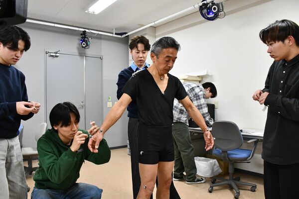 大場さん（中央）の体に赤外線反射マーカーを貼り付ける学生たち＝２０２５年１２月２５日午前、大田原市北金丸