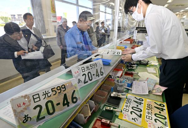 窓口で真新しい日光ナンバーを受け取る男性=7日午前9時30分、宇都宮市八千代1丁目