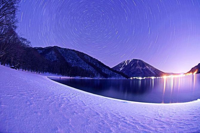 雪に覆われた中禅寺湖南岸の阿世潟。夜、北極星を中心に光跡を描く北の空を仰ぐ（約３０分露光）
