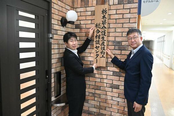 センターの看板を掲げる伊藤センター長（右）と岩佐部長＝１８日午前、宇都宮市若草１丁目