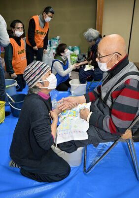 避難生活が続く佐野さんに足湯を提供し、手を握って励ます本県ボランティアの菊池さん（手前左）＝28日午前10時20分、石川県穴水町中居ロ