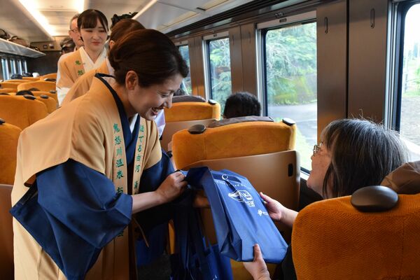 プレミアムシートの乗客に記念品を手渡す女将ら＝15日午後３時50分、日光市