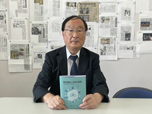 芸術文化地域連携センターの15年の歩みをまとめた書籍を手にする長島重夫センター長＝９月上旬、宇都宮市上戸祭４丁目