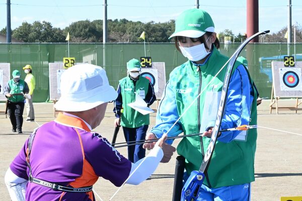 選手に矢を手渡すボランティアの高校生（右）＝30日午前、那須烏山市緑地運動公園多目的競技場
