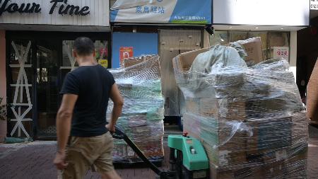 香港の街中に設置された宅配便の引き取り拠点の前で、山積みの荷物を運ぶ作業員=10月2日