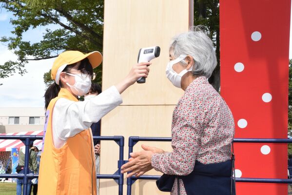 来場者の検温をする本国体の最年少ボランティアの今野さん（左）＝８日午後、宇都宮市の県総合運動公園「いちご一会広場」