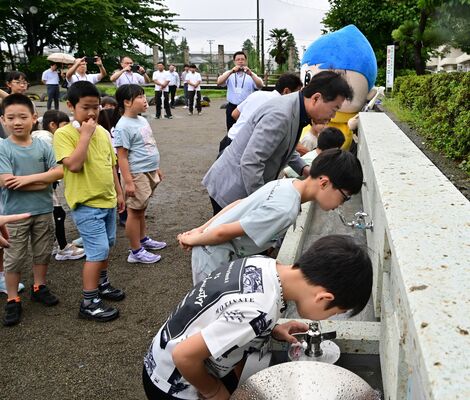 宮の泉で水を飲む児童たち