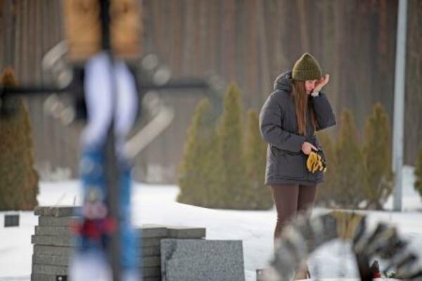 ロシアのウクライナ侵攻開始から4年となった24日、首都キーウ近郊イルピンにある夫デニスさんの墓の前で涙をぬぐうイアナ・サクンさん(共同)