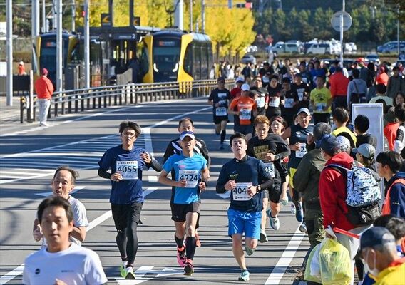 ライトラインが行き交うそばを力走するランナーたち＝19日午前10時15分、宇都宮市清原工業団地
