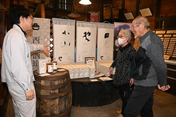 蔵直売所の販売日、来訪客にウイスキーの特性を説明する西堀哲也専務(左)=10月25日午前、小山市