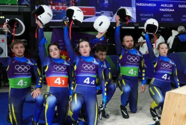 　リュージュのチームリレーで、ゴール後に片膝をついてヘルメットを掲げるウクライナ代表の選手たち＝コルティナダンペッツォ（ロイター＝共同）