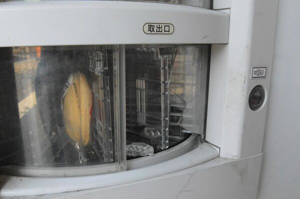 取り出し口が破損した自動販売機＝21日午前、那珂川町三輪
