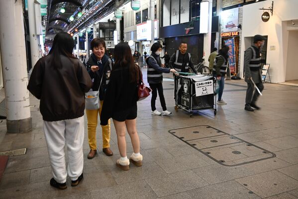 揃いのベストを着用し、オリオン通りでごみ拾いをしながら若者に声をかけるボランティアら＝22日夜、宇都宮市