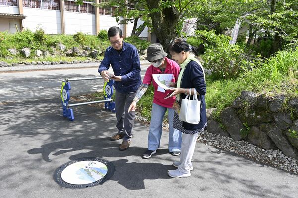 大関和をイメージしたキャラクター「チカちゃん」をデザインしたマンホールを観光客に説明するメンバー（中央）