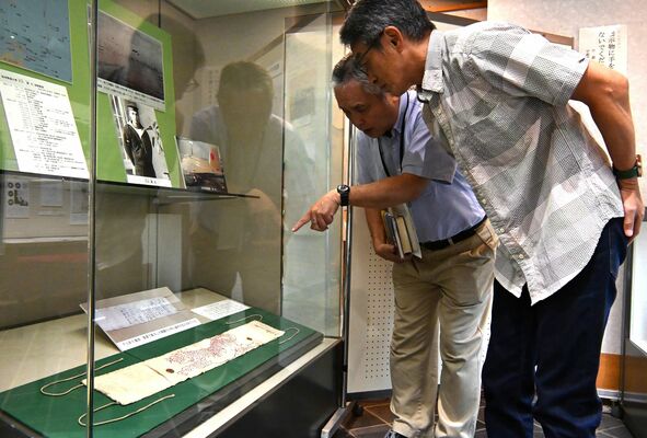 展示された亡き義父の千人針を前に、大塚さん(左)から説明を受ける吉成さん=10日午前、宇都宮市本丸町