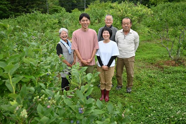 色付き始めたブルーベリーの畑で笑顔を見せる安藤さん夫妻（手前）と、旧生産者たち