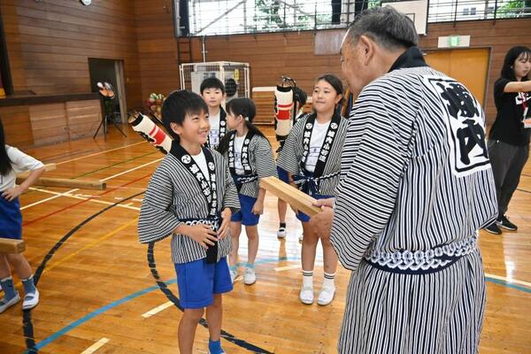荒川会長(右)から拍子木の打ち方を教わる児童