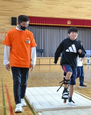 義足歩行を体験する児童（右）