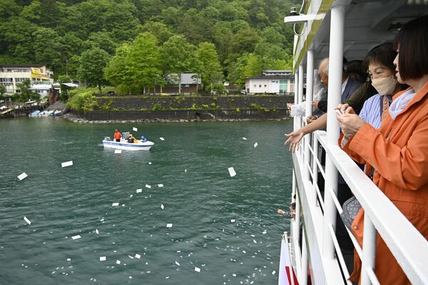 お札を湖面に流す参列者たち