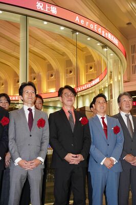 上場を祝うディスプレーの前で記念撮影する森西社長（左から２人目）＝４日午前、東京都内