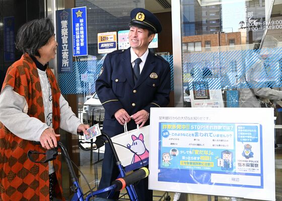 ＡＴＭで表示を始めたデモ画面（右下）を使って利用客（左）に詐欺の手口を説明する警察官＝４日午前、宇都宮市桜４丁目