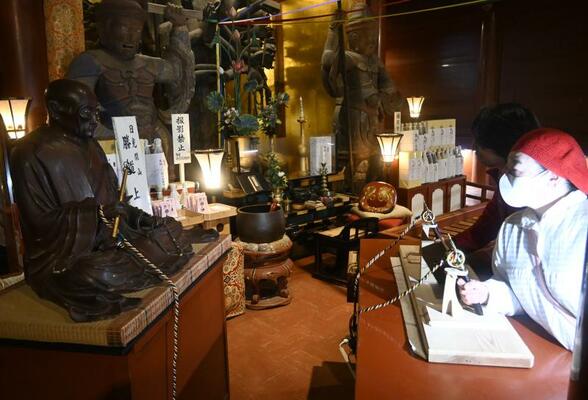 坐像の手首とロープでつながった錫杖を握る参拝客