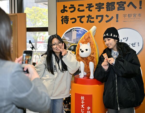 餃子犬じゅうべえ像と記念撮影する観光客=1日午前11時30分、JR宇都宮駅