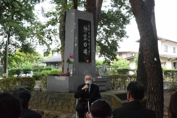 慰霊碑の前であいさつする県被団協元会長の中村さん＝19日午前、宇都宮市西川田４丁目