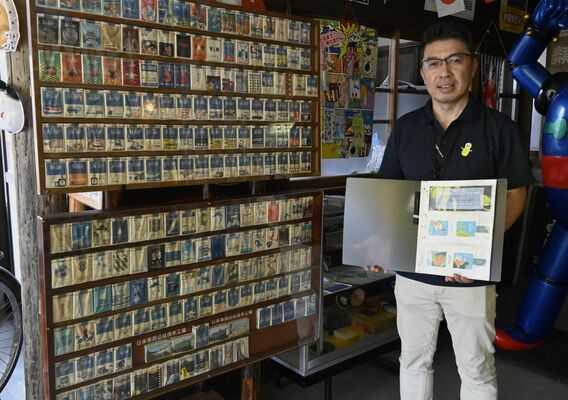 ハイライトの額装と広告付きの箱をまとめたファイルを持つ滝田課長