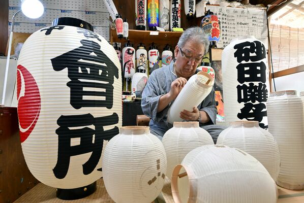 提灯が並ぶ作業場で筆を入れる田中さん＝４日午前10時55分、栃木市藤岡町新波