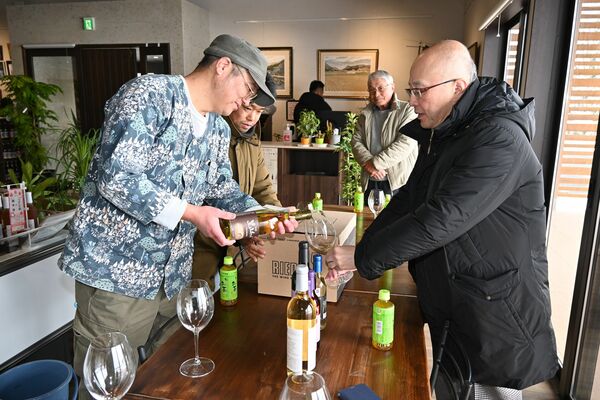 栽培・製造担当の荒井誠之さん（左）から「かぬま里山わいん」をグラスにそそいでもらう鈴木さん＝２月８日、鹿沼市下奈良部町