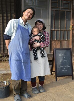 古民家の自宅に民泊とパンの店の看板を掲げた君島さん夫婦と、集落に27年ぶりに生まれた赤ちゃんの琉生ちゃん