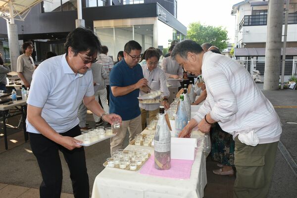 銘柄ブラインドした一升瓶から注がれたカップグラスの日本酒を受け取る参加者＝５月１６日、さくら市