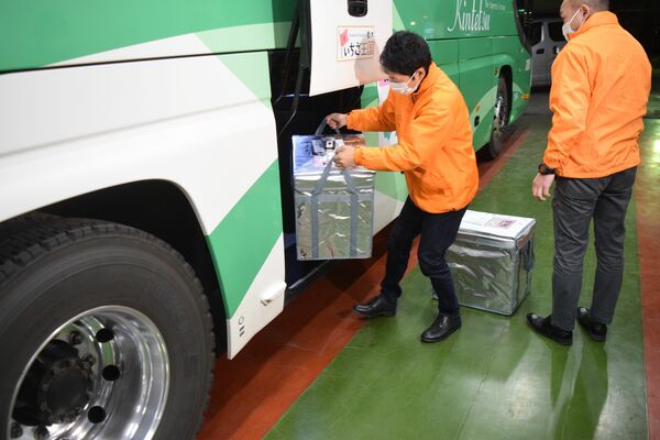 イチゴ入りの保冷バッグをバスのトランクルームに積み込む関係者