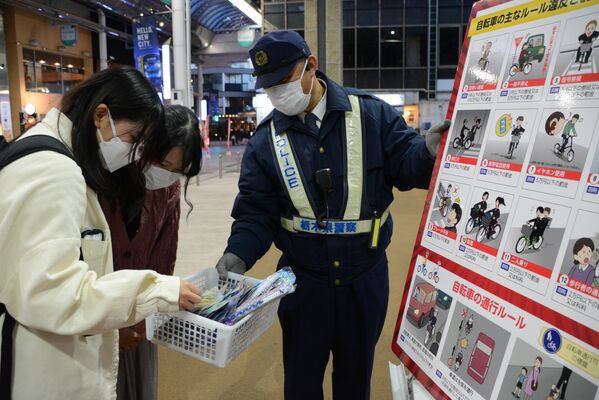 通行人に反射材などを配る警察官（右端）＝８日午後、宇都宮市江野町