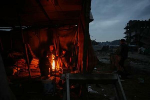 イスラエル軍の攻撃で破壊された跡で、たき火で暖をとる人たち=12日、ガザ(AP=共同)