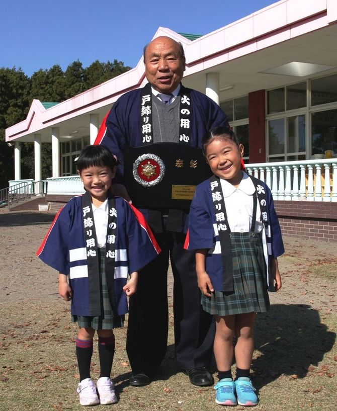 総務大臣表彰の盾を持つ鈴木園長（中央）。年長組の坂井さん（右）、濱さん（左）。