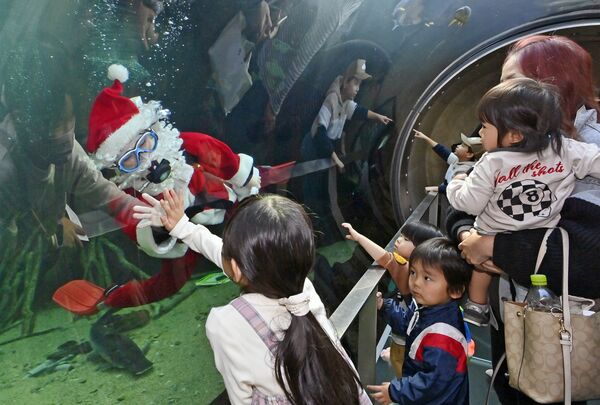 ガラス越しに子どもたちと手を合わせる水中マスク姿のサンタクロース＝７日午前11時25分、大田原市佐良土