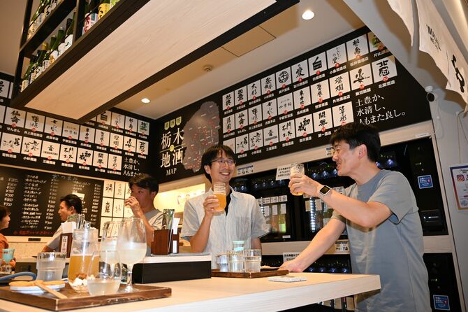 ビールを飲みながら談笑する男性客。壁の上には「栃木地酒（日本酒）」銘柄が紹介されている＝２９日夕、嶋田屋酒店宮みらい店角打ち店舗