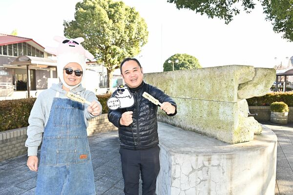 シウマイ像の前で棒シウマイを掲げる大房さん（右）と福田さん