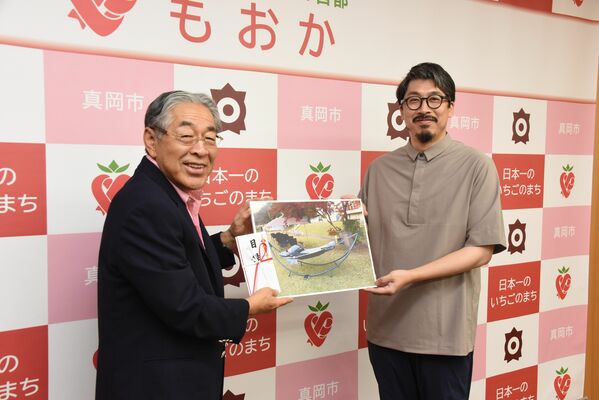 石坂市長にハンモックの写真パネルなどを渡す井上さん（右）
