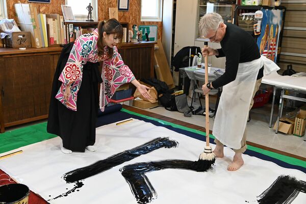 さおりさん(左)の指導を受けながら大筆で文字を書く参加者