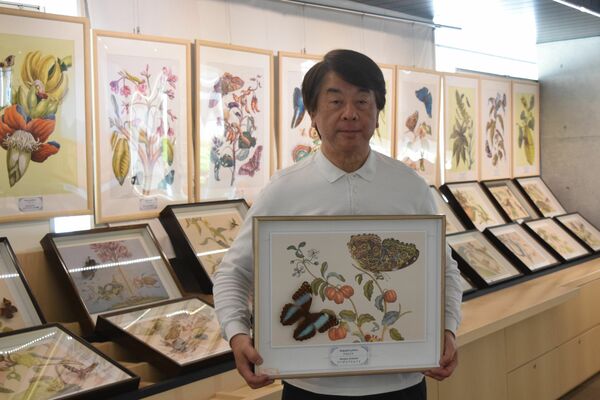 図版と標本を収めた標本箱を持つ新部さん