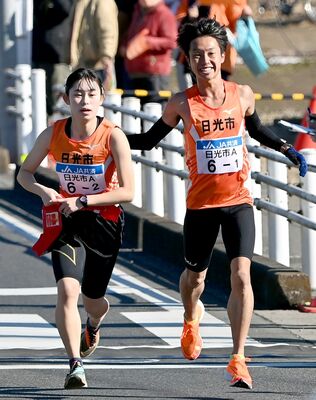 １区区間賞に輝いた日光Ａの梶谷（右）が笑顔で２区の選手にたすきをつなぐ＝宇都宮市