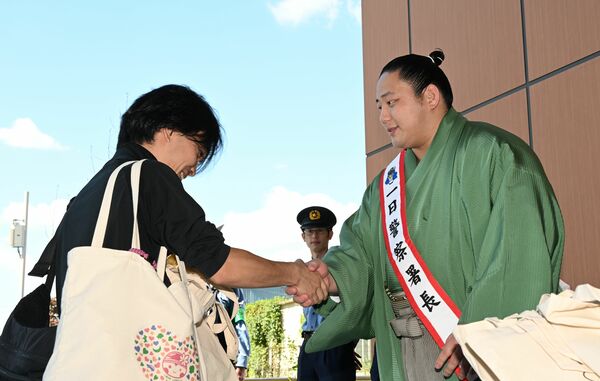 来場者と握手する三田関(右)=10日午前、宇都宮市一条1丁目