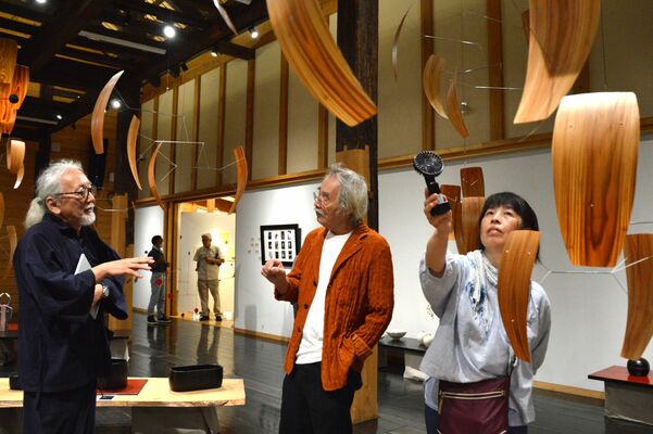 元酒蔵の会場の梁からつるされたモビール。松崎代表と語り合うサトウさん（左）