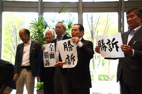 「勝訴」と書かれた紙を掲げて喜ぶ原告側の住民ら＝18日午後１時35分、東京都千代田区