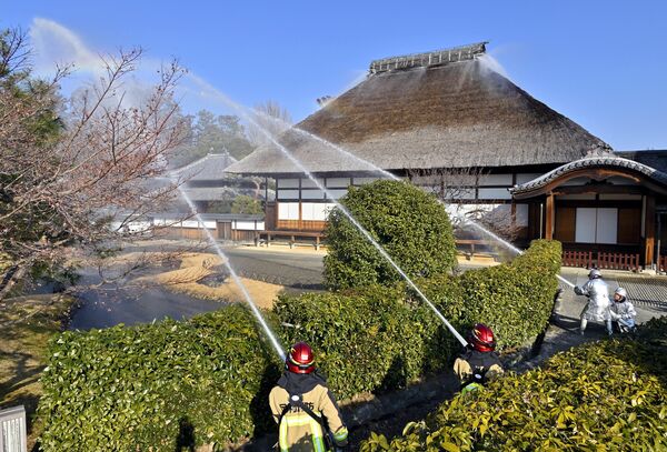 放水する消防署員らと屋根から水が噴き出る方丈=24日午前、足利市昌平町