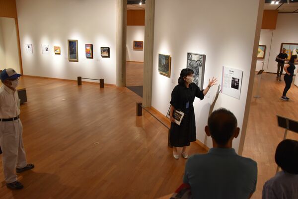 ギャラリートークで作品を解説する清水学芸員（中央奥）＝16日午前、日光市山内